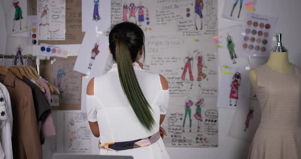 Professional fashion designer woman contemplating drawings in studio