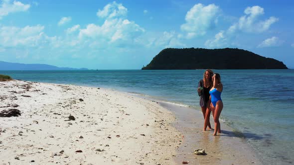 Young smiling ladies on holiday having fun at the beach on summer white sand and blue 4K background