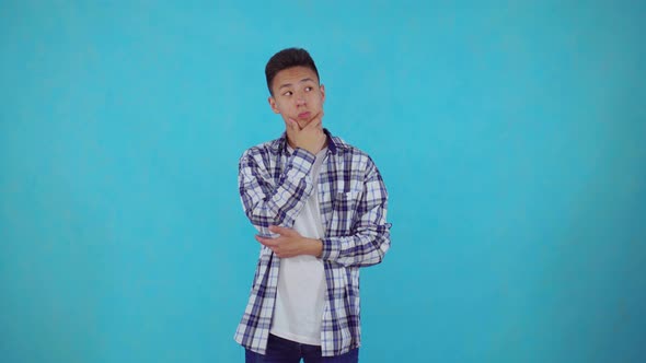Thoughtful Young Asian Man on Blue Background