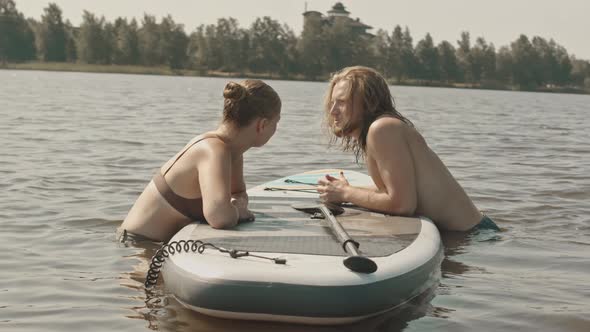 Couple Chatting in Lake Leaning on Sup Board