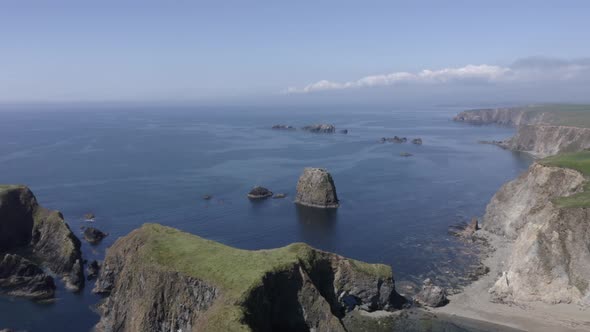 Aerial flyover of sea stack rocks off rugged calm ocean coastline