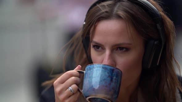 Portrait of a Sad Young Woman Listening To Music Using Headphones Outdoors. Sitting on an Autumn