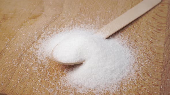 Wooden spoon of white sugar on a wooden surface