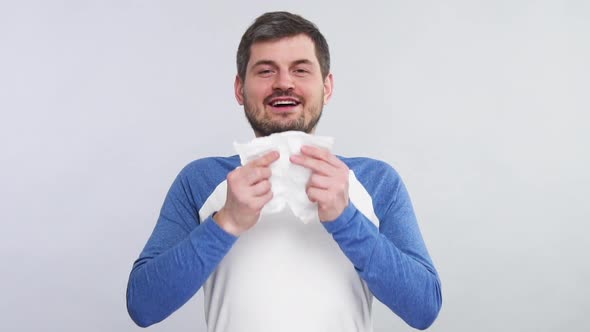 Happy Young Bearded Man Sneeze Into His White Tissue Isolated on Grey Background