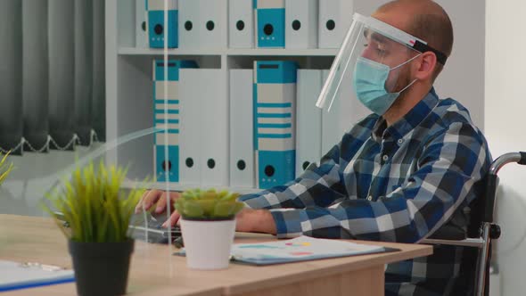 Disabled Businessman with Face Protection Working on Computer