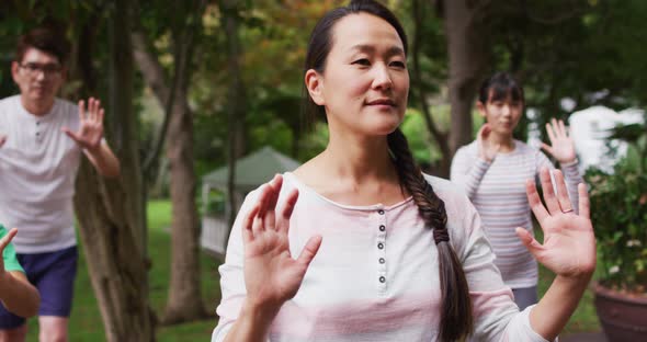 Happy asian parents exercising in garden with son and daughter, practicing tai chi together