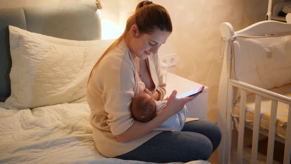 Panning Shot of Mother Using Smartphone Giving Breast To Her Hungry Baby Son on Bed at Night