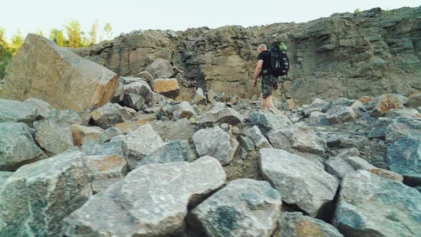 traveler in sportswear with a backpack on his shoulders is going on a pile of stones