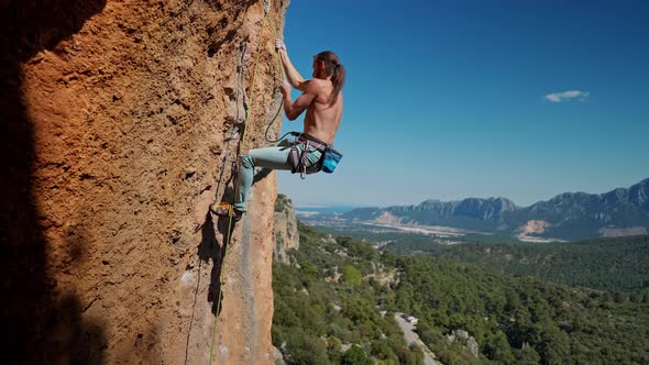 Strong and Muscular Fit Rock Climber Climbs By Rope on Vertical Cliff