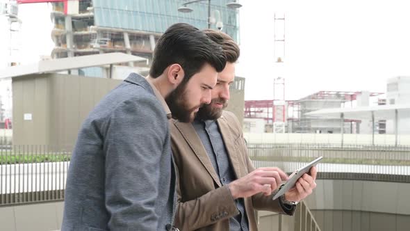 Two young bearded men outdoor discussing using digital tablet