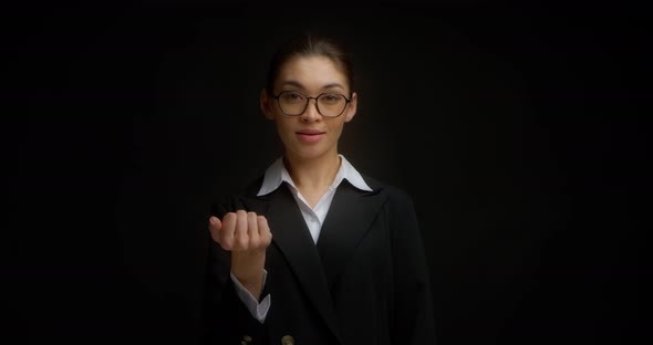 Businesswoman in Glasses and a Black Jacket Shows a Come Here Hand Gesture