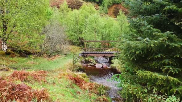 Cinematic drone zoom out shot of scottish highland creek with little bridge in background