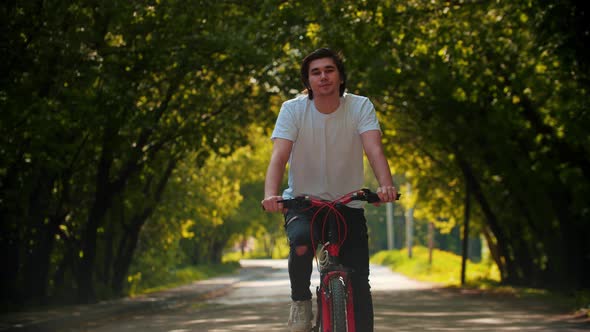Young Man in White Shirt Riding a Bike and Stops To Drink Water