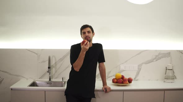 Young Man Eating Red Apple at Home in the Kitchen