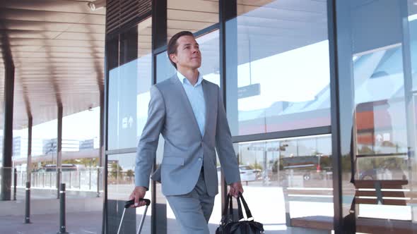 Elegant businessman walking with suitcase along the airport. Young mail entrepreneur.