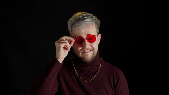 Handsome Man in Stylish Blouse Taking Off Red Sunglasses Facial Expression on Black Background