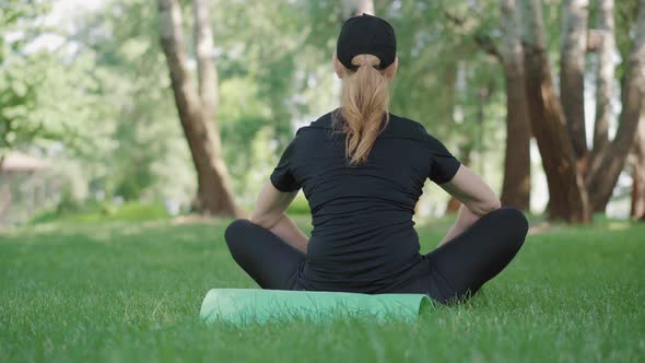 Back View of Mid-adult Sportswoman Sitting on Exercise Mat and Breathing. Female Caucasian Yogi