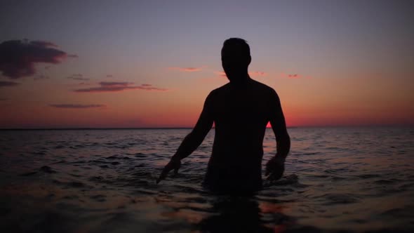 Silhouette of Cheerful Strong Man Taking Pleasure and Dancing in Water After Swimming in Sea During