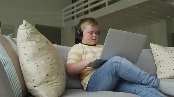 Caucasian boy sitting in living room and using laptop alone at home