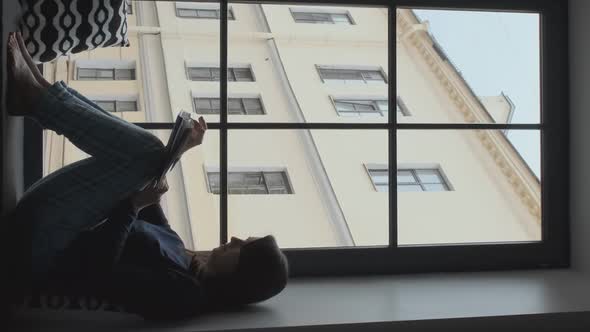 Silhouette of Woman Reads Book on Windowsill