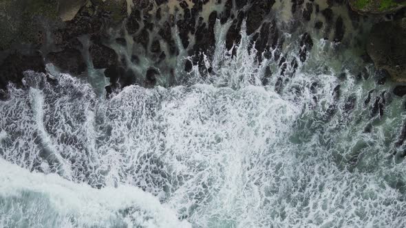 Top down aerial view of giant ocean waves crashing and foaming in coral beach