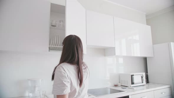 Young Woman Opens the Door and Takes Out Glass Cups From Cabinet