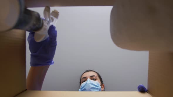 Woman in Mask Packing Box with Cleaning Supplies