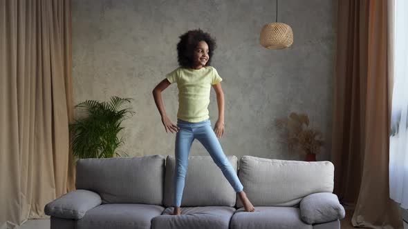 Portrait Little Cheerful African American Girl Dancing and Jumping on the Couch