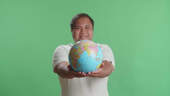 Smiling Asian Man In Front Of Green Screen Background Hand In The World Globe To The Camera