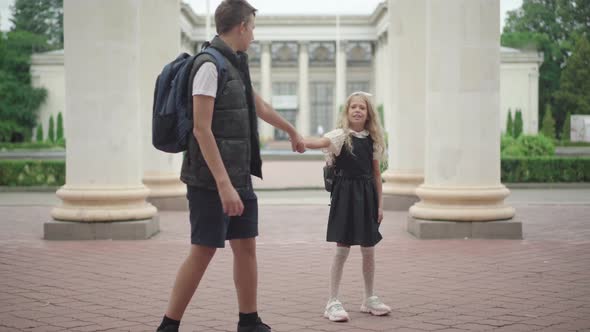 Wide Shot Portrait of Schoolboy Pulling Hand of Stubborn Schoolgirl Unwilling To Go To Studying