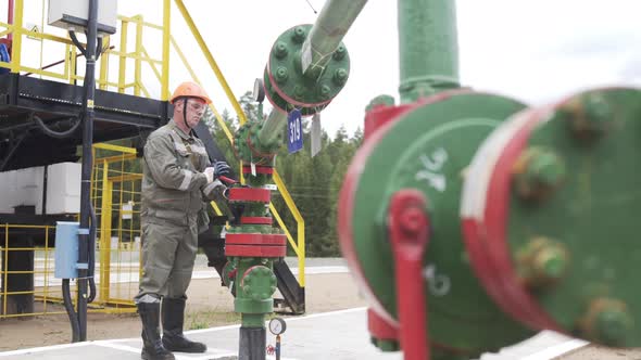 Oilman in Orange Helmet and Protective Glass Closing Valve of X-mass Wellhead To Shut Off Well