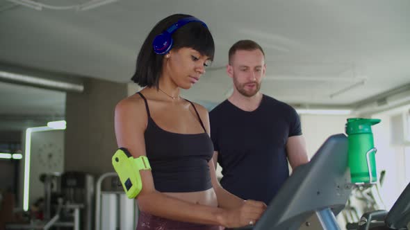 Fitness Trainer Helps Woman To Use Treadmill in Gym