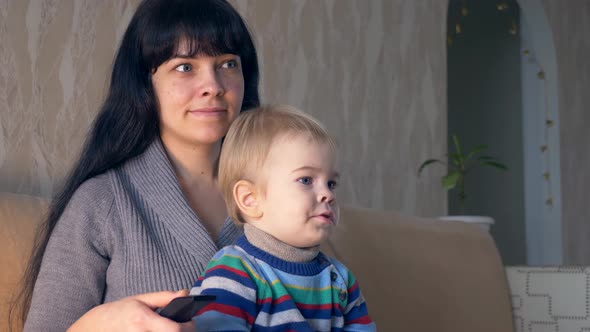 Pretty Mother With Remote Control in Hand and Cute Child Watching Personal Home Video