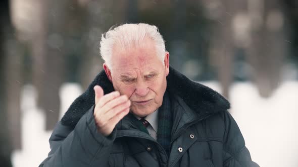 An Old Man Standing Outdoors While Snowfall - Touching His Head