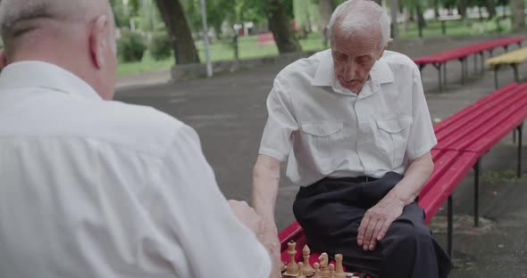 Two Male Pensioners Spend Leisure Time on a Street Bench Talk and Play Chess