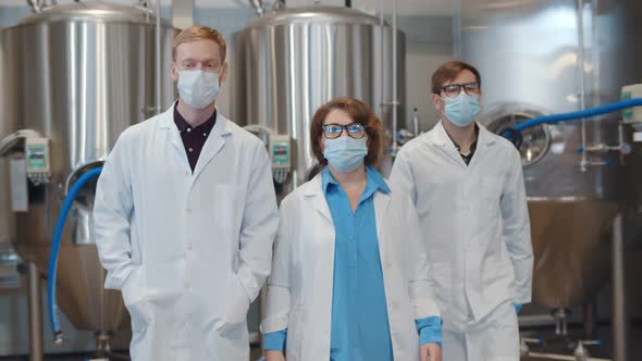 Scientists Team in Safety Mask and Lab Coats Walking in Large Beer Factory