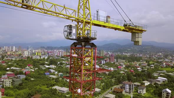 Construction crane on construction site against backdrop of mountains and city.
