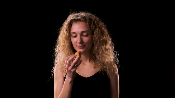 Pretty Blonde Woman with Long Curly Hair Takes Bite of Croissant and Rolls Her Eyes in Pleasure