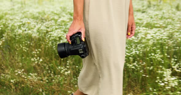 Unrecognizable woman hold digital camera in her hands on flower field landscape