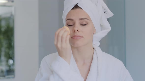 Attractive young brunette Woman in bathrobe  applying foundation with beauty blender