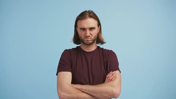 Young Longhaired Man Has Folded His Hands Grimacing and Looking Offended or Upset While Posing on