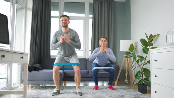 Caucasian Couple is Doing Squats and Leg Swings with Elastic Band at Home in Cozy Bright Room