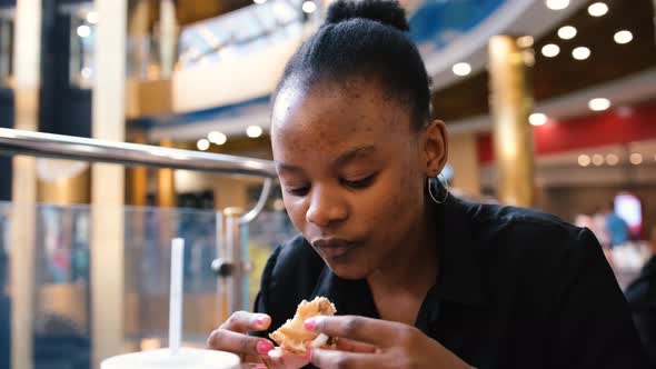 Beautiful Young Black Woman Eating Fast Food in a Restaurant Enjoying Delicious Juicy Hamburger