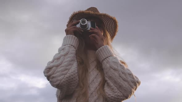 Blond Woman Using Vintage Camera Under Cloudy Sky