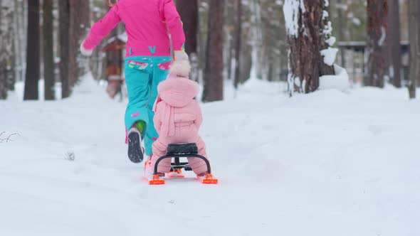 Young Woman Runs Along White Snowy Forest Path Carrying Sled