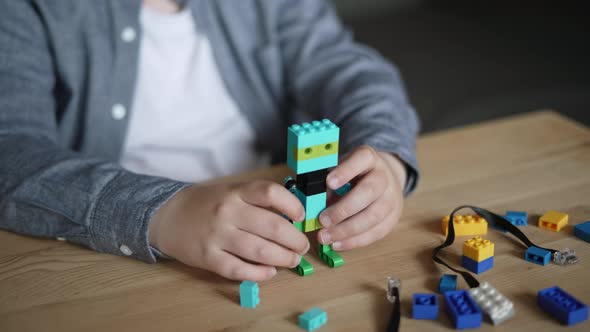 Caucasian Child Plays with Toy Doll From Constructor on Wooden Table Closeup