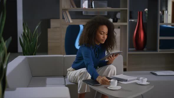 African American Woman Using Tablet Scrolling Social Media in Home Office Cafe