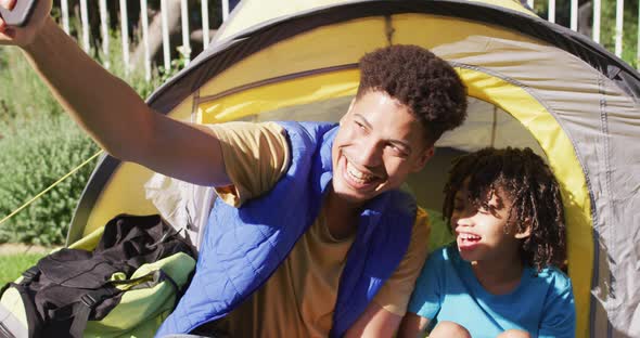 Happy biracial man and his son taking selfies using smartphone in garden