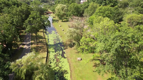 An aerial drone view over a park in Valley Stream, NY with a reflective stream and pond. It is a sun