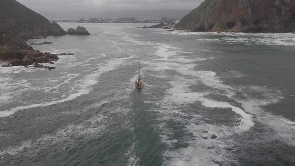 Ship crosses foamy Knysna River bar in silvery overcast conditions